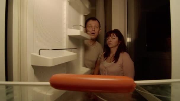 Le couple marié ouvre le réfrigérateur, il est presque vide, ils sont surpris, la femme attrape la saucisse en premier - Séquence, vidéo