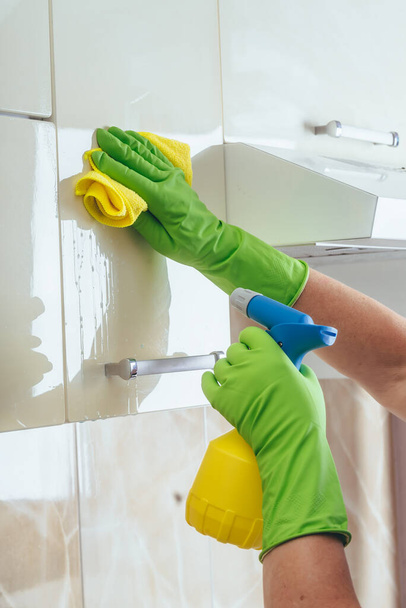 A woman wipes a yellow cloth kitchen cabinet, using a chemical from a bottle. Cleaning of the apartment. Light kitchen. kitchen cabinet. - 写真・画像