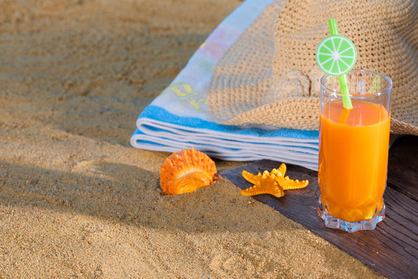 Fresh orange fruit juice stands in a glass with a straw. A beach towel lies on the sandy beach. - Foto, immagini