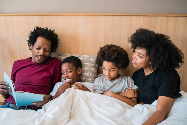 Portrait of happy African American family reading a book on bed in the bedroom at home. Lifestyle and family concept - Фото, изображение