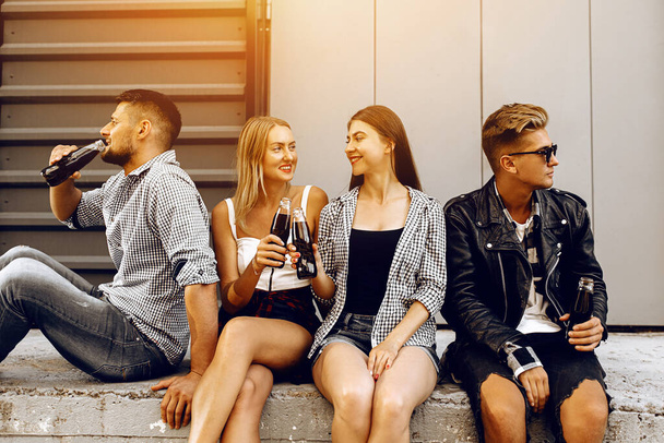 Jóvenes amigos con estilo caminan, los estudiantes se divierten y beben bebidas sentados en los escalones de la ciudad
 - Foto, imagen
