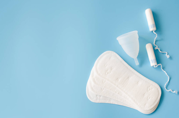 Egészségügyi pad, menstruációs csésze és tamponok kék háttérrel. A női higiénia fogalma a menstruáció alatt. - Fotó, kép