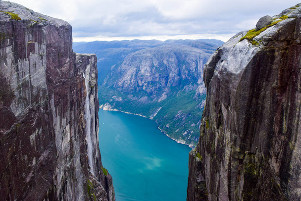 Pohled na Lysefjorden přes trhlinu mezi dvěma útesy 984 metrů vysoké, kde se v blízkosti zasekl slavný Kjeragbolten - nejnebezpečnější kámen na světě. Mountain Kjerag, Rogaland County, Norway. - Fotografie, Obrázek
