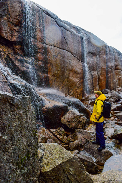 Tourist man looks at waterfalls falling from cliffs near trail to the Kjeragbolten is the most dangerous stone in the world. The boulder stuck at an altitude of 984 meters above Lysefjorden. Norway. - Photo, Image