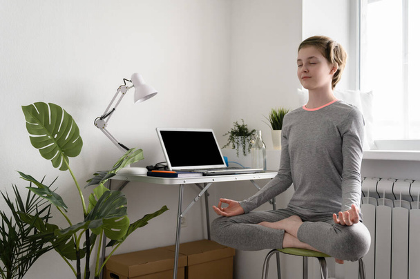 Nastolatka trenuje w domu, ćwiczy jogę, siedzi w pozycji lotosu, medytuje. - Zdjęcie, obraz