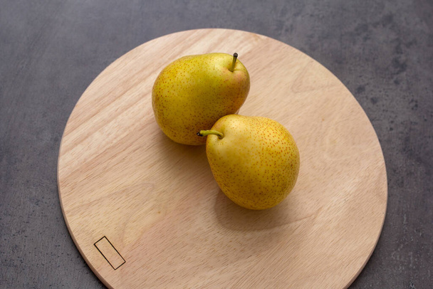 テーブルの上のまな板の上に黄色い梨が2つ. - 写真・画像