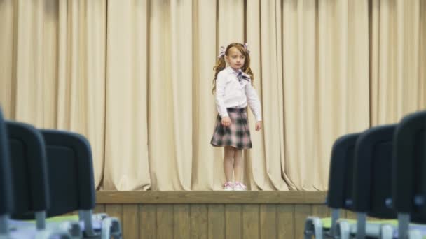 Mała dziewczynka na scenie w holu bez ludzi. Dziewczyna obraca się wokół siebie.. - Materiał filmowy, wideo
