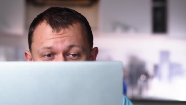 A man in surprise raises his eyebrows, reads news on the Internet in his laptop - Materiał filmowy, wideo
