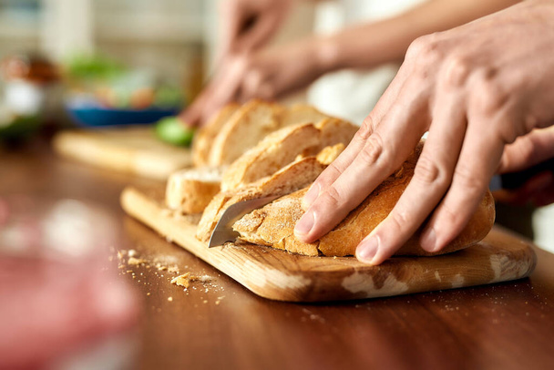 Close up of male hands cutting tasty homemade bread on the wooden board. Vegetarianism, healthy food concept. - Foto, immagini