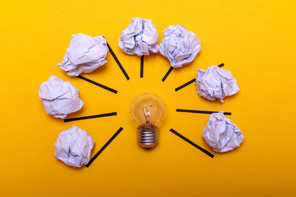 Inspiration concept crumpled paper and light bulb metaphor for good idea. White crumpled paper and light bulb on yellow background, flat lay. - Foto, Bild