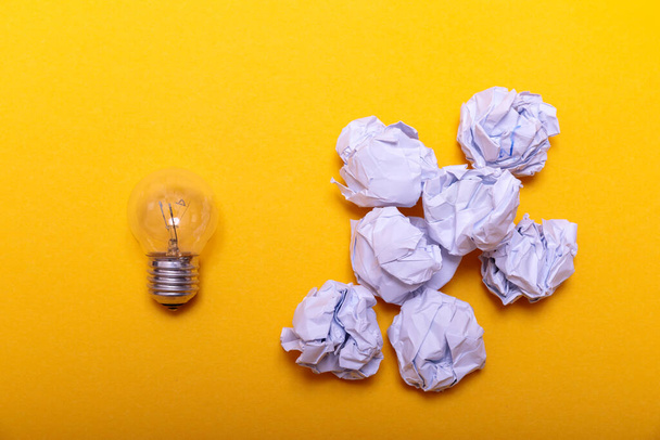 Inspiration concept crumpled paper and light bulb metaphor for good idea. White crumpled paper and light bulb on yellow background, flat lay. - Photo, Image