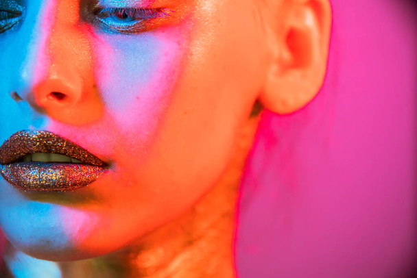 Fashion model metallic silver lips and face woman in neon uv blue and purple lights, posing in studio, beautiful girl, glowing make-up, colorful make up.  - Фото, изображение