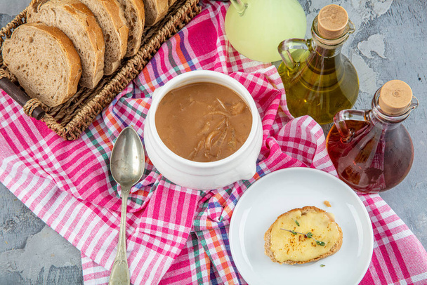 Διάσημο γαλλικό πιάτο, γαλλική κρεμμυδόσουπα. Καραμελωμένα κρεμμύδια μαγειρεμένα σε ζωμό με κρασί και βότανα, συμπληρωμένα με φρυγανισμένη μπαγκέτα και τυρί και τελειωμένα κάτω από τη σχάρα. - Φωτογραφία, εικόνα