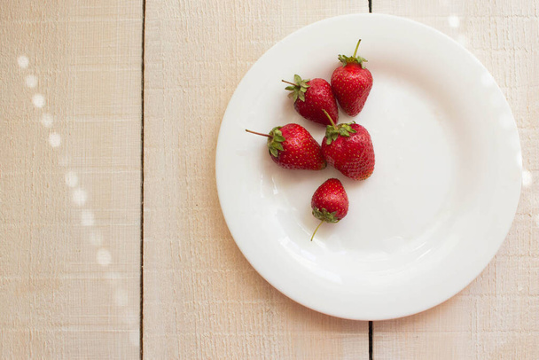 Η έννοια της καλοκαιρινής και υγιεινής καλοκαιρινής τροφής. Φρέσκα εποχιακά μούρα με βιταμίνες. Πέντε λαμπερές φράουλες κοντά σε λευκό ξύλινο φόντο. - Φωτογραφία, εικόνα