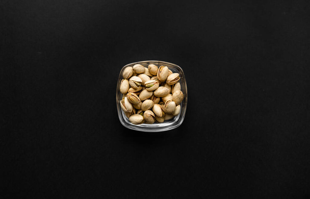 Pistachios in a small plate on a black table. Pistachio is a healthy vegetarian protein nutritious food. Natural nuts snacks. - Photo, image