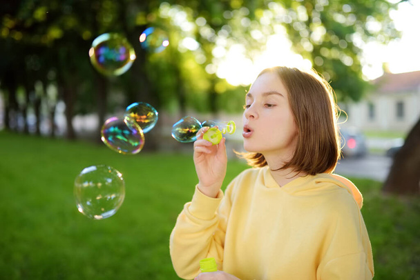 Pretty teenage girl blowing soap bubbles on a sunset. Child having fun in a park in summer. Funny activities for kids. - Fotografie, Obrázek