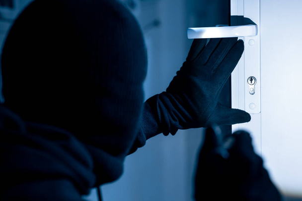 Robber in black balaclava cracking door with metal picklock - Photo, Image