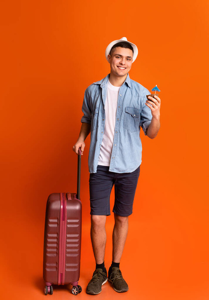 Молодий хлопець турист з багажем тримає екзотичний коктейль
 - Фото, зображення
