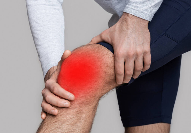 Knieblessure of ontsteking. Man in sportkleding drukt zijn handen tot de knie rood gemarkeerd - Foto, afbeelding