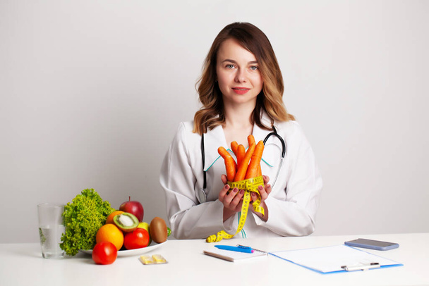 Молодий дієтолог у консалтинговій залі за столом зі свіжими овочами та фруктами, працює над дієтичним планом
 - Фото, зображення