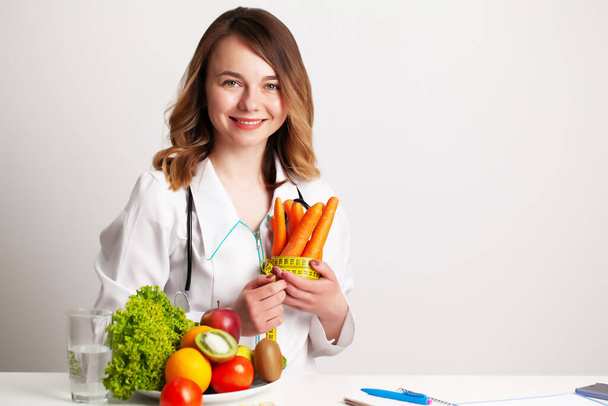 Mladý dietní lékař v ordinaci u stolu s čerstvou zeleninou a ovocem, pracuje na dietním plánu - Fotografie, Obrázek