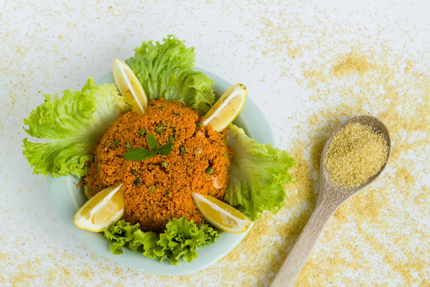 Traditional Turkish Kisir "Bulgur" salad on wooden plate with lemon slice,lettuce and wooden spoons in grains. - Photo, Image