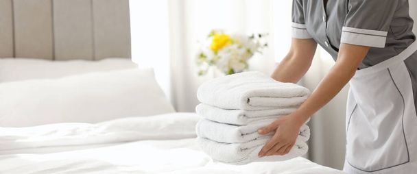 Young chambermaid putting stack of fresh towels in bedroom, closeup view with space for text. Banner design - Фото, изображение