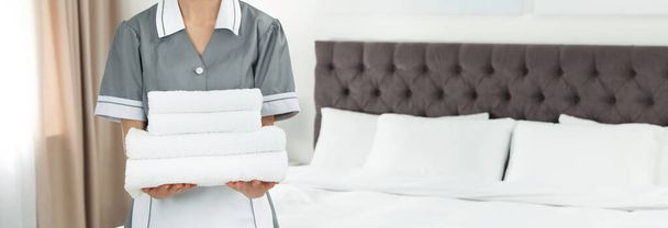 Chambermaid holding stack of fresh towels in hotel room, closeup view with space for text. Banner design - Φωτογραφία, εικόνα