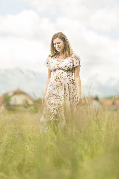 Beautiful pregnant woman in white summer dress in meadow full of yellow blooming flowers. - Foto, imagen