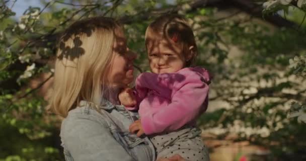 Ładna kobieta trzyma swoją córeczkę na rękach w letnim parku - Materiał filmowy, wideo