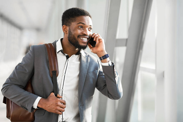 Cheerful Businessman Talking On Phone Walking With Backpack In Airport - Photo, Image