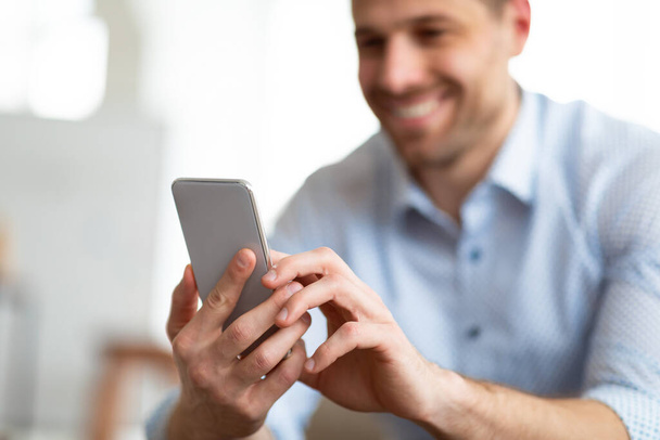 Hombre adulto alegre usando el teléfono inteligente en casa - Foto, imagen