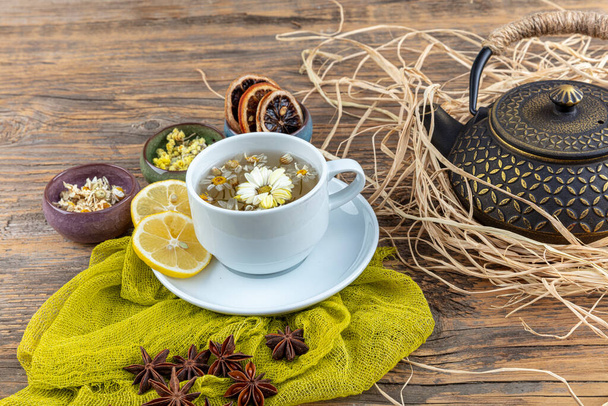 Heřmánkový čaj v lité konvici. Heřmánkový šálek čaje, starožitná čínská litinová konvice, citron a hvězdný anýz na dřevěném stole. - Fotografie, Obrázek