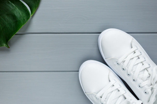 Close up Witte vrouwelijke sneakers op grijze houten ondergrond. Vlakke lay, bovenaanzicht, minimale achtergrond. Tijdschrift of mode blog concept - Foto, afbeelding