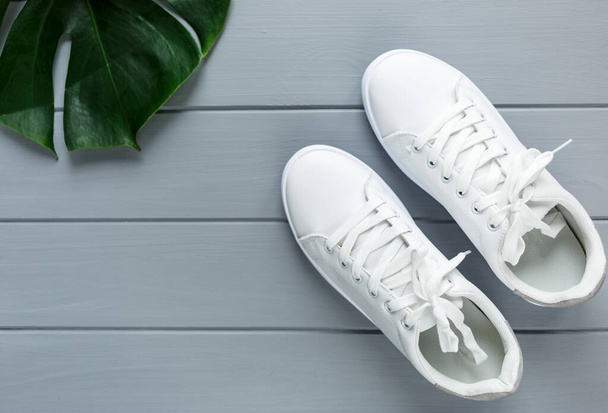 Κοντινό πλάνο Λευκά γυναικεία αθλητικά παπούτσια σε γκρι ξύλινο φόντο. Επίπεδο lay, κορυφαία θέα, ελάχιστο φόντο. Έννοια περιοδικού ή fashion blog - Φωτογραφία, εικόνα