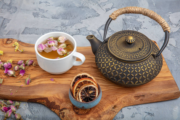 Martwa natura z tradycyjną azjatycką herbatą ziołową przygotowaną w zabytkowym żeliwnym czajniku z organicznymi suchymi ziołami na rustykalnym drewnianym stole. Filtr wsteczny. - Zdjęcie, obraz