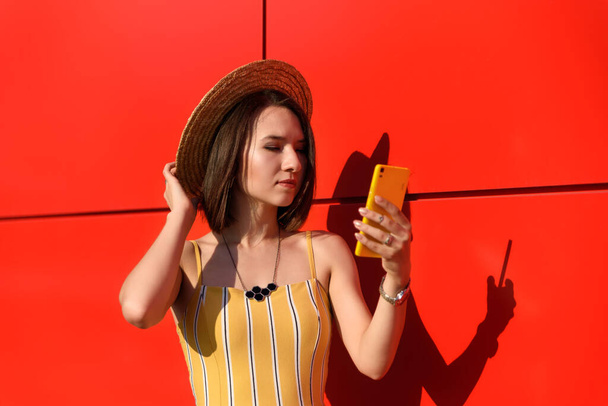 slender girl posing against a red wall with a phone - Photo, Image