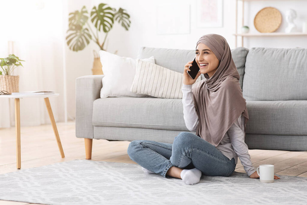 Czas wolny. Radosna muzułmanka rozmawiająca przez komórkę z przyjacielem w domu - Zdjęcie, obraz