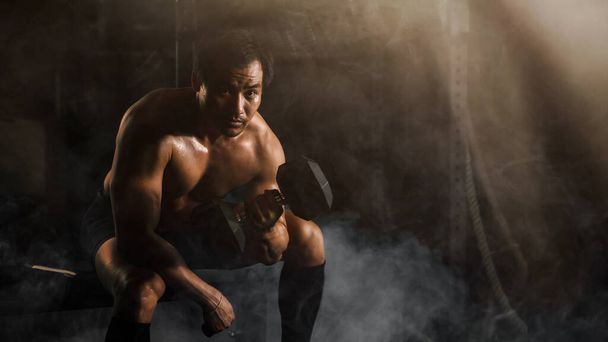 portrait of asian athletic bodybuilding man sitting on bench workout and exercise by lifting dumbbell with on hand in gym and fitness club in dark tone - Photo, image