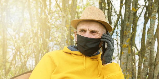 pensioner in facial mask and gloves talks on phone in garden - Fotó, kép