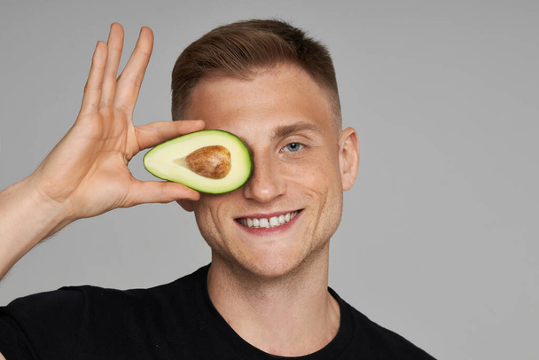  Avocado for the face. Skin care using natural vitamins. Male model holds fresh fruits near the face and smiles. - 写真・画像