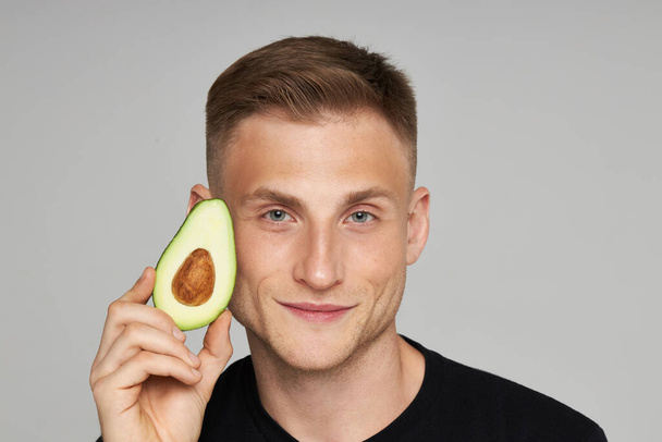 Avocado for the face. Skin care using natural vitamins. Male model holds fresh fruits near the face. - 写真・画像