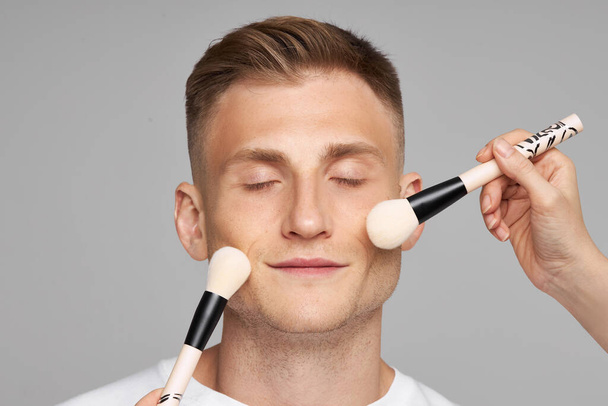  Mens makeup. Facial beauty treatments with cosmetics. Female hands with Touch Mans Face brushes with foundation. - Valokuva, kuva
