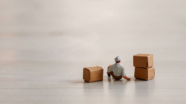 Der Rücken eines sitzenden Arbeiters. Miniaturmenschen und Schachtel. - Foto, Bild