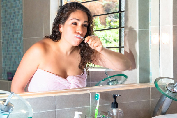 Dişlerini fırçalayan ve banyoda aynaya bakan gerçek bir kadın. Diş sağlığı hizmetleri - Fotoğraf, Görsel