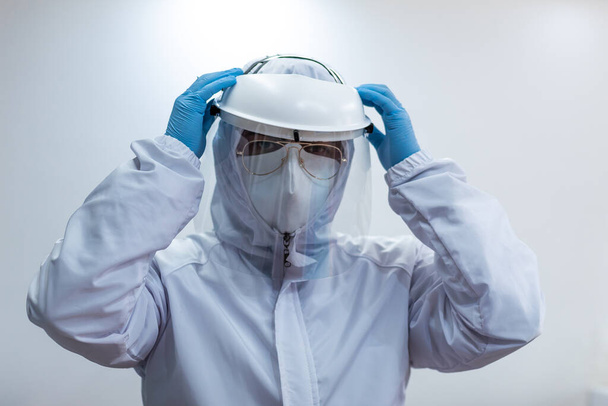 Médico vestindo terno de biossegurança branca, protetor facial, máscara e luvas
 - Foto, Imagem