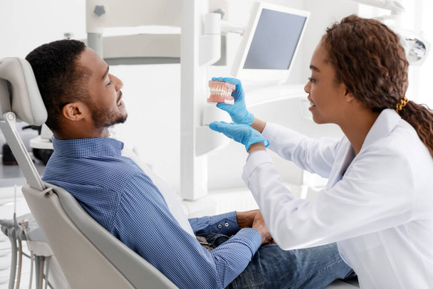 Female stomatologist and black guy looking at plastic jaw - Photo, image
