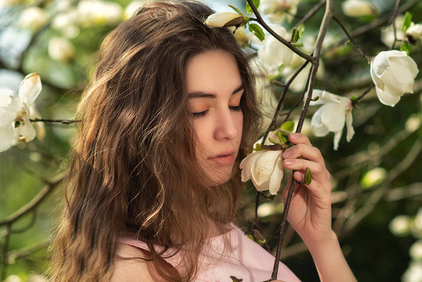 Красивая молодая женщина наслаждается природой в весенних цветах магнолии. Красивая девушка в саду с цветущими деревьями магнолии. Мечтающая девушка с цветущими цветами на открытом воздухе. Модельный портрет
 - Фото, изображение