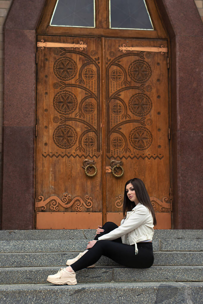 Young beautiful woman sits on stair near old doors - Zdjęcie, obraz