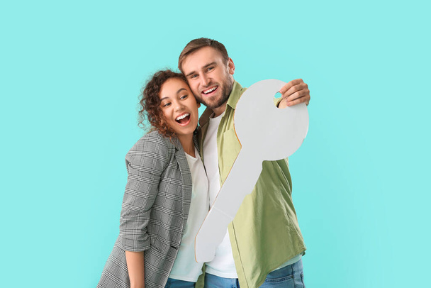Happy young couple with big paper key on color background - Foto, imagen